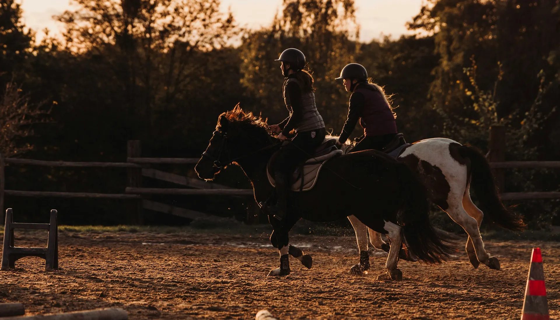 Two riders in an arena at sunset